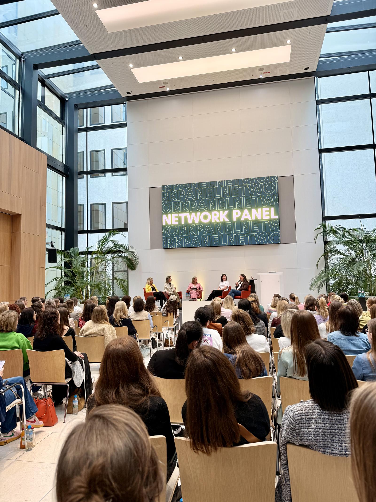 Publikum bei einem Network Panel in einem lichtdurchfluteten Atrium